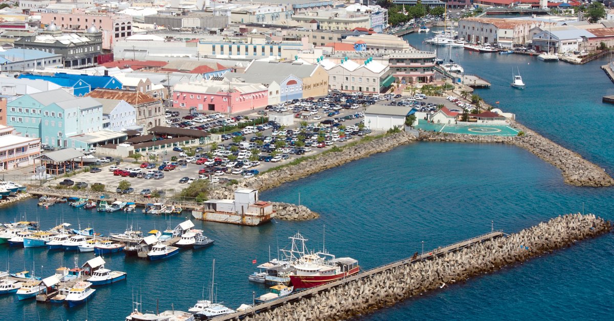 Many colorful buildings sit along a waterfront, and many boats are floating in a nearby marina with retaining walls.